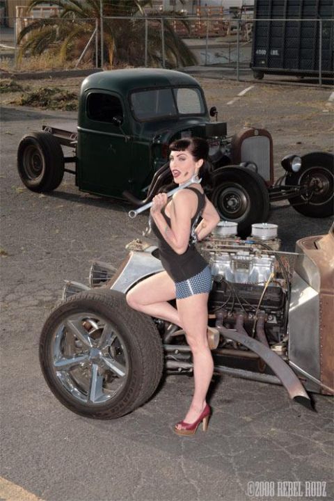1992 Ford Bronco - A woman poses with a wrench next to a hot rod truck, with another vintage truck in the background.