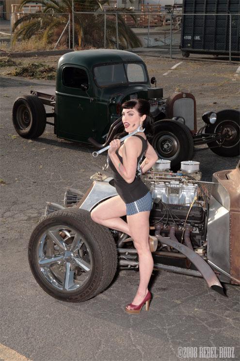 Hot rod truck with exposed engine and a woman posing with a wrench