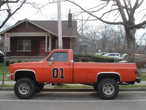1991 Ford Crown Victoria - Side view of an orange pickup truck with "01" on the door and lifted suspension.