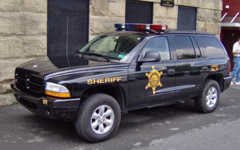 1991 Ford Crown Victoria - A black SUV with 'SHERIFF' text and emergency lights is parked outside a building.