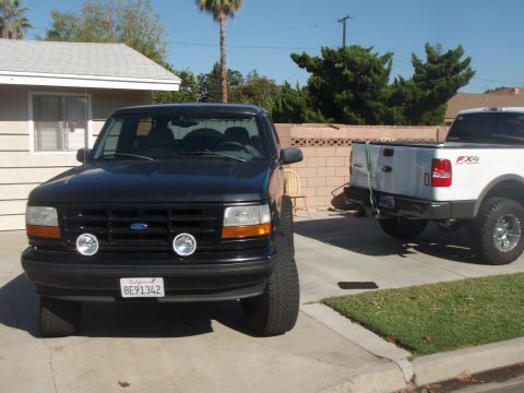 1995 Ford Bronco - A black 1995 Ford Bronco is parked in a driveway next to a white pickup truck.
