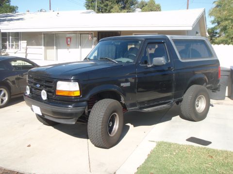 1995 Ford Bronco - Black 1995 Ford Bronco with aftermarket wheels and tires parked outside a house.