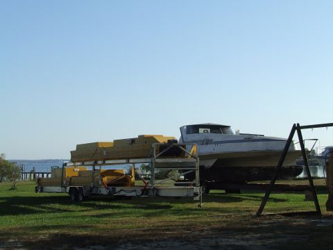 1976 Ford F-150 - A boat is parked on a trailer, loaded with lumber, in a grassy area with a clear blue sky overhead.