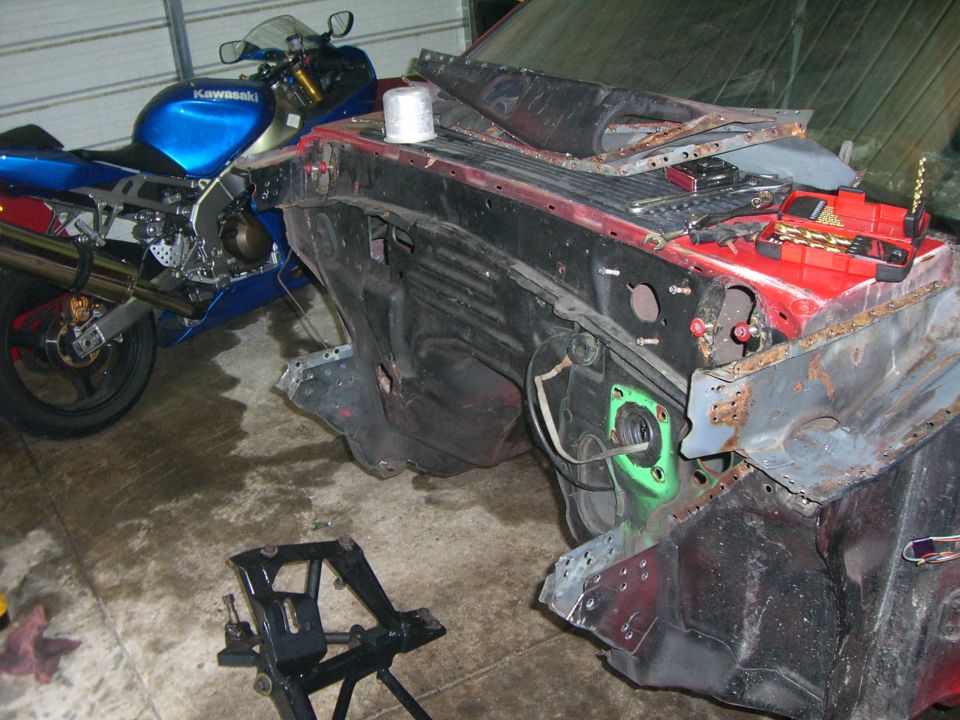 Disassembled vehicle front end with a blue Kawasaki motorcycle parked nearby