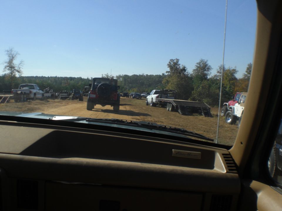 View from inside a vehicle looking out at a field with several off-road vehicles and trailers
