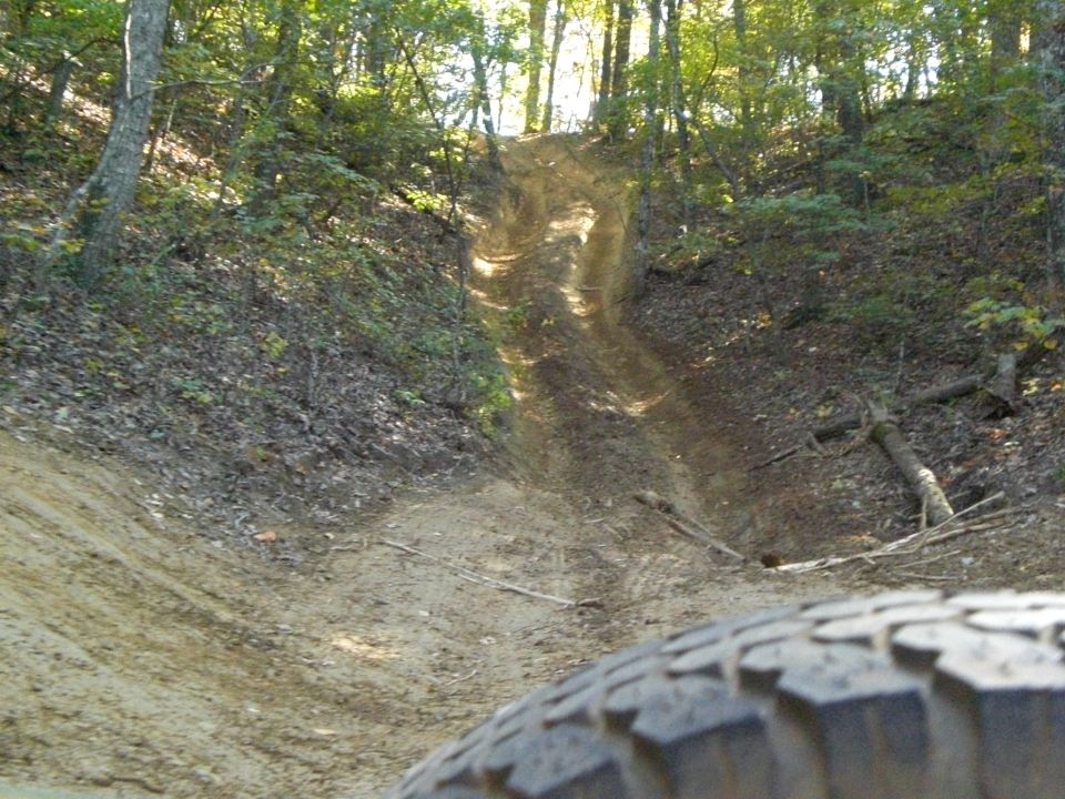 Tire in foreground on dirt trail going uphill through woods