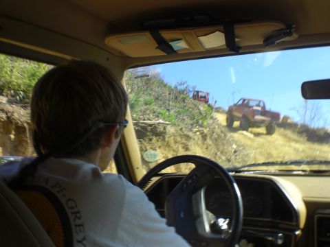 1989 Ford Bronco - Two trucks navigate a steep, off-road trail under a clear blue sky.