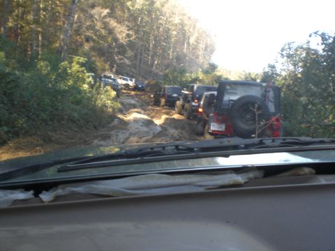 1989 Ford Bronco - Several off-road vehicles are stuck on a muddy trail in a wooded area.