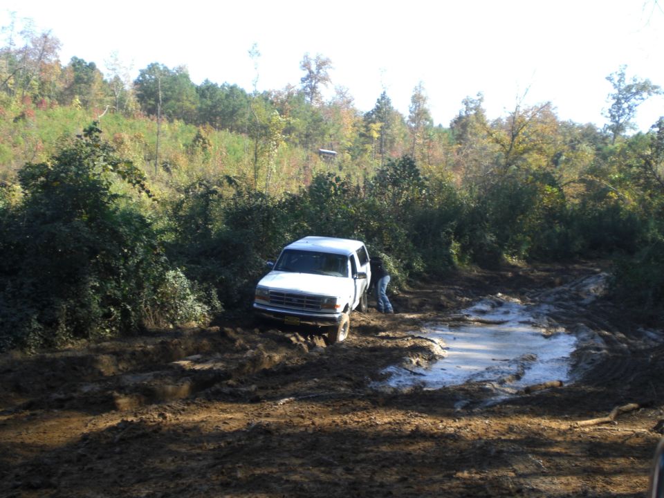 White SUV stuck in a muddy trail with a person trying to help