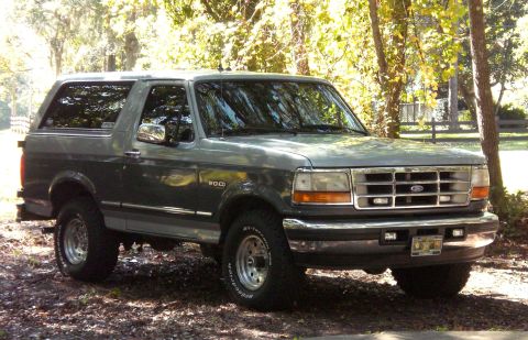 1996 Ford Bronco - A 1996 Ford Bronco is parked on a dirt road surrounded by trees.
