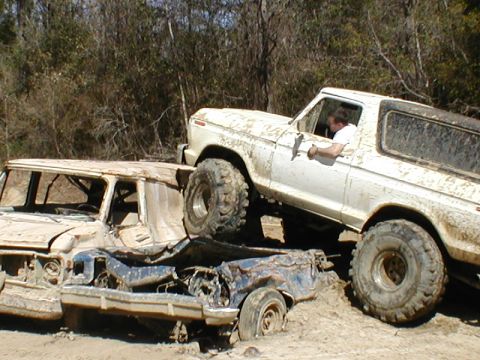 1979 Ford Bronco - A white 1978 Ford Bronco navigates over a wrecked blue vehicle in a muddy, off-road environment.