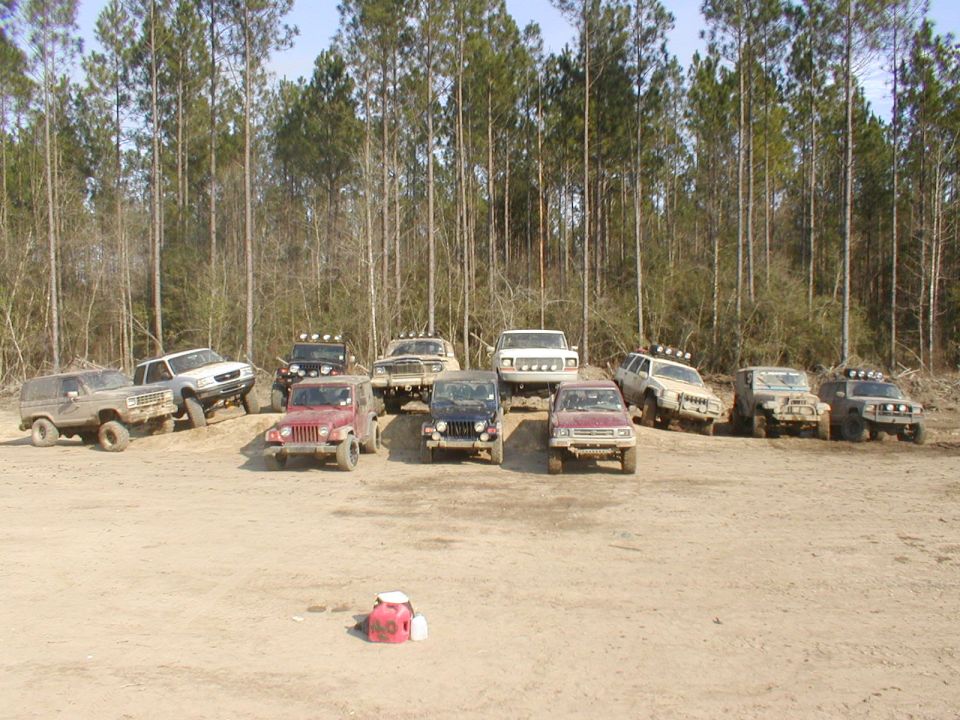 Several off-road vehicles parked on dirt with trees in background
