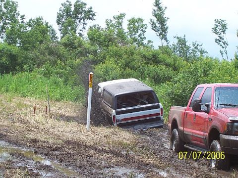 1979 Ford Bronco - A vehicle is stuck in the mud with a red pickup truck nearby.