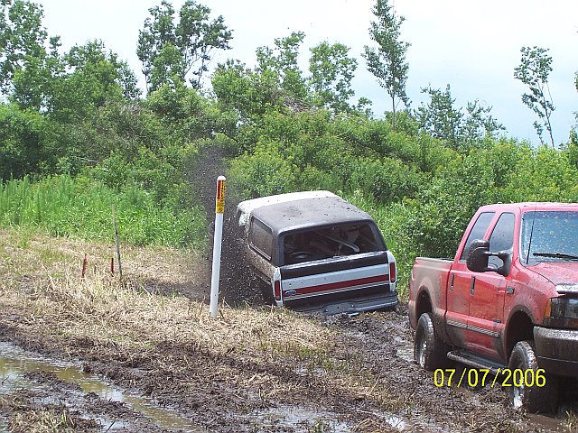 off-road vehicle stuck in mud next to a red pickup truck