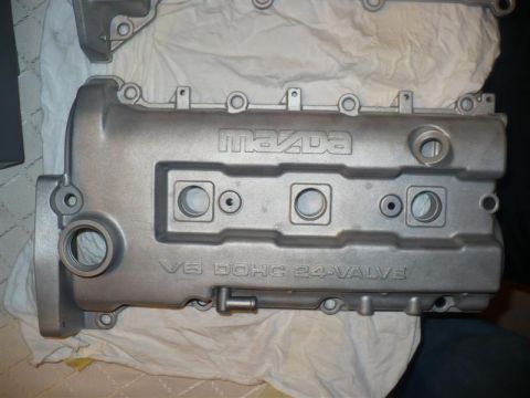 1993 Ford Probe - A silver-colored engine part with "MAZDA" and "V6 DOHC 24-VALVE" inscribed on it sits on a white cloth.