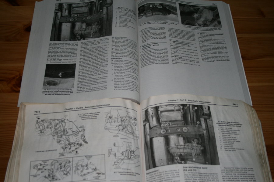 Open vehicle repair manual with diagrams and text on wooden surface