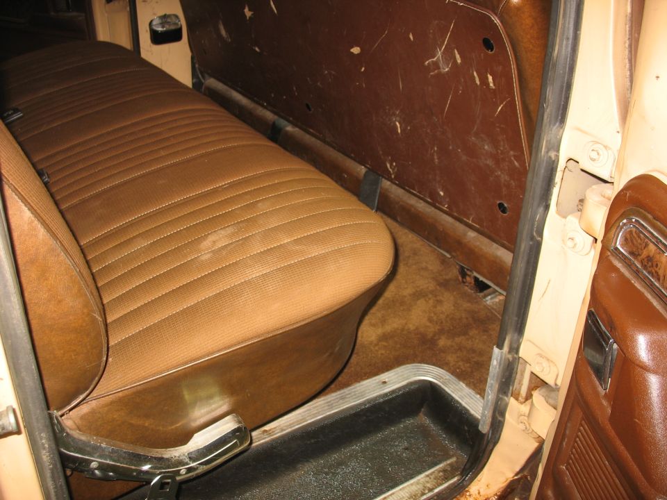 Interior shot of a truck's bench seat and door panel. The seat is brown with horizontal pleats. The door panel is also brown and shows some wear