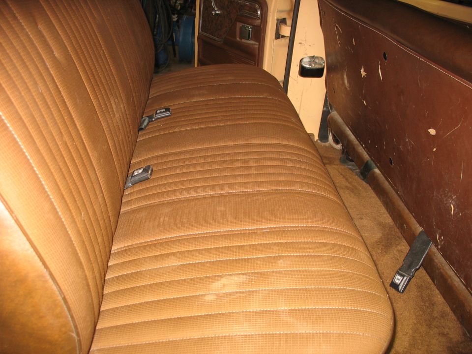 Brown vinyl bench seat with seatbelts inside a vehicle. The seat has horizontal stitching and some stains