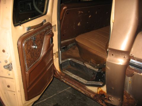 1978 Ford F-250 - The interior of a 1978 Ford F-250 pickup truck, tan and brown upholstery and door panels, with visible rust on the exterior rocker panel.
