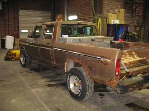 1978 Ford F-250 - This heavily rusted crew cab pickup truck, likely from the 1970s, is parked indoors with a snow plow attachment nearby.