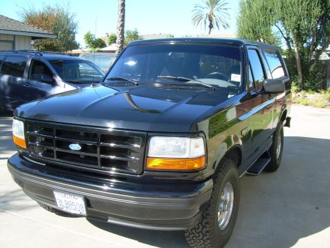 1986 Ford Bronco - Black Ford Bronco parked in a driveway with a palm tree in the background. Another vehicle is visible to the left.