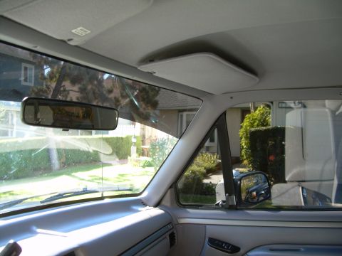 1986 Ford Bronco - View from inside a vehicle, looking out at a residential street scene through the windshield and side window.