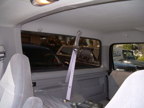1986 Ford Bronco - View from inside a vehicle, looking out the windows at other cars and a house in the background.