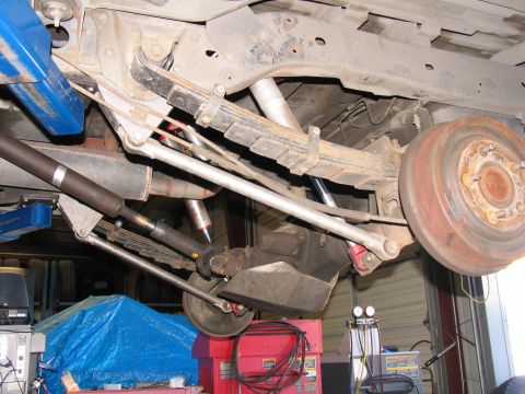 1984 Ford Bronco - The rear suspension and axle components of a vehicle are shown from underneath, underneath, in a workshop setting that appears to be a repa…