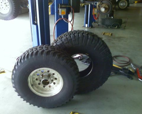 1992 Ford Bronco - Two large off-road tires and wheels are staged in a repair shop, possibly for installation.