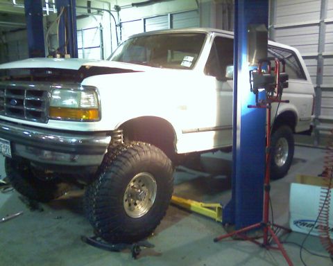 1992 Ford Bronco - This white SUV is on a lift in a garage with its hood open, showing off its large tires.