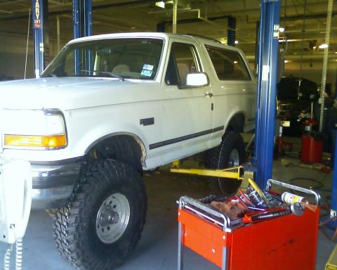 1992 Ford Bronco - A white 1992 Ford Bronco is shown on a car lift in a garage, undergoing modifications.