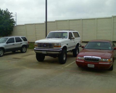 1992 Ford Bronco - A white Ford Bronco is parked in a lot next to a red Mercury Grand Marquis and a silver SUV.