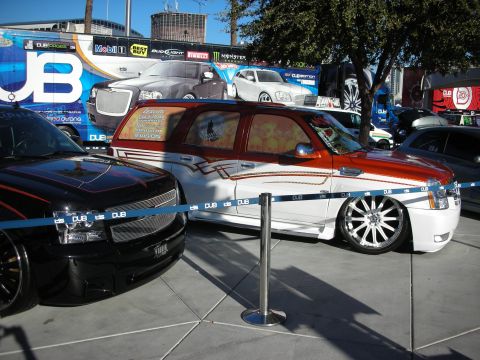 1998 Ford Crown Victoria - Two customized SUVs are on display, with a large banner advertisements for various vehicles behind them.