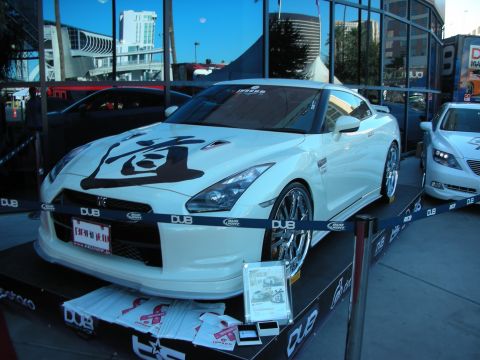 1998 Ford Crown Victoria - A white Nissan GT-R is displayed on a platform with other vehicles in the background.