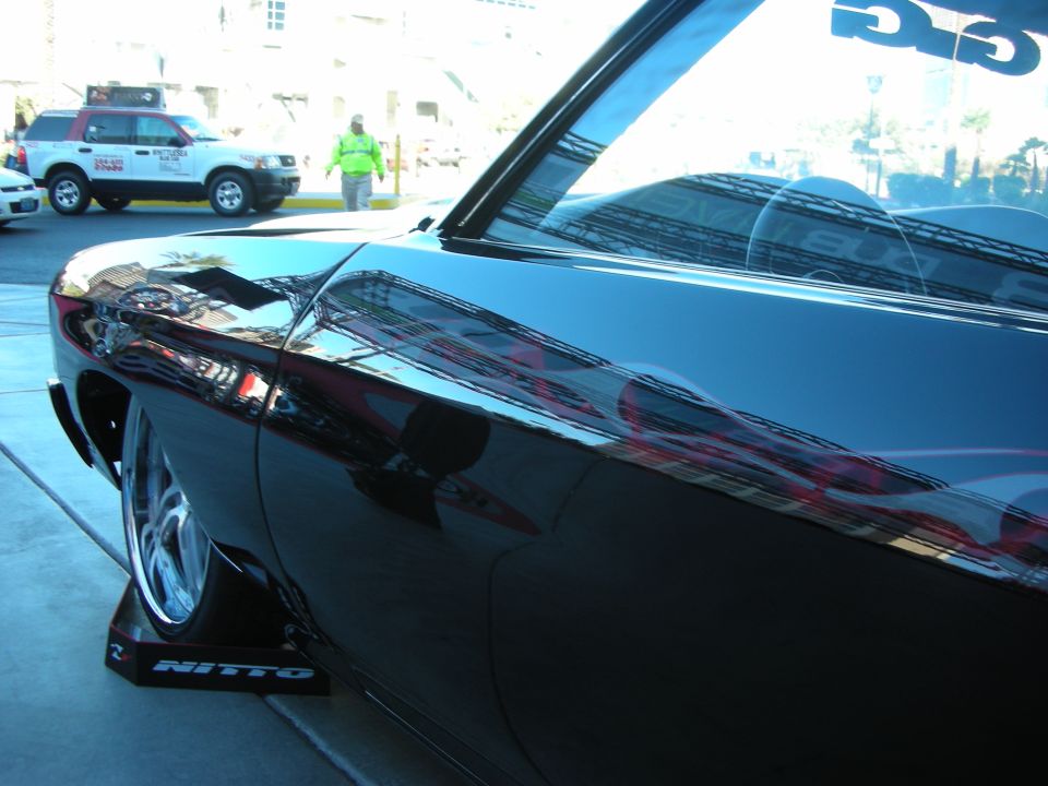 Black car with flame graphics on its side, parked on Nitto stands. Another SUV is visible in the background