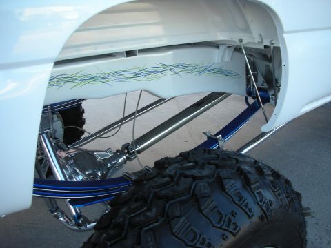 1998 Ford Crown Victoria - Close-up of a lifted white pickup truck's rear suspension, custom pinstriping and a large off-road tire.