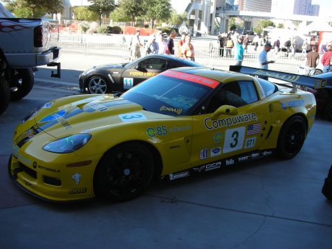 1998 Ford Crown Victoria - A yellow racing Corvette with sponsor decals is parked at an outdoor event.