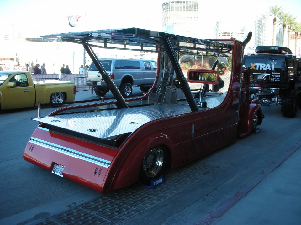 custom red tow truck with a flatbed, parked next to a yellow pickup and a black SUV with 'XTRAIL' on it