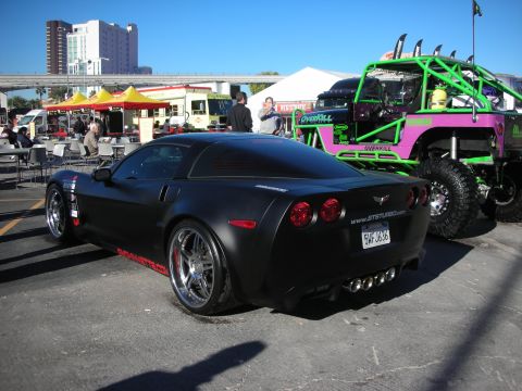 1998 Ford Crown Victoria - A matte black Chevrolet Corvette is parked outdoors, with a custom off-road vehicle visible behind it.