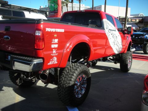 1998 Ford Crown Victoria - A lifted red Ford truck with custom decals is parked outdoors, with another lifted vehicle in the background.