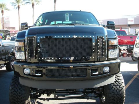 1998 Ford Crown Victoria - Front view of a black pickup truck with a custom grille and prominent tires, seen at an outdoor event.