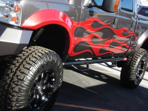 1998 Ford Crown Victoria - A customized truck with flame decals and large tires is parked on asphalt.