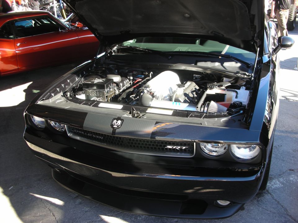 Black Dodge Challenger SRT with hood open, showing engine. Red car in background