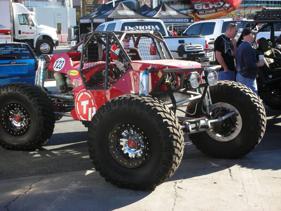 Red off-road buggy with large tires and roll cage, parked outdoors