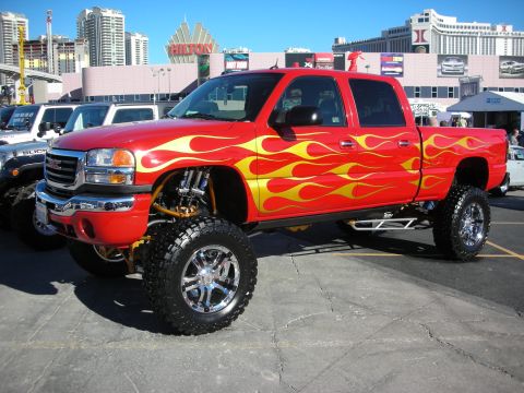 1998 Ford Crown Victoria - Customized red GMC pickup truck with flame graphics and an extreme lift kit is parked outdoors.