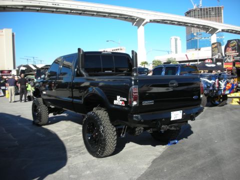 1998 Ford Crown Victoria - A modified black Ford F-250 Super Duty truck is displayed outdoors with other vehicles and structures in the background.