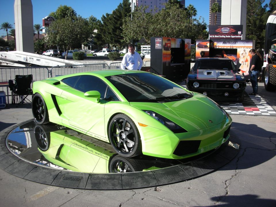 Lime green sports car on a rotating display platform, with a black classic car behind it