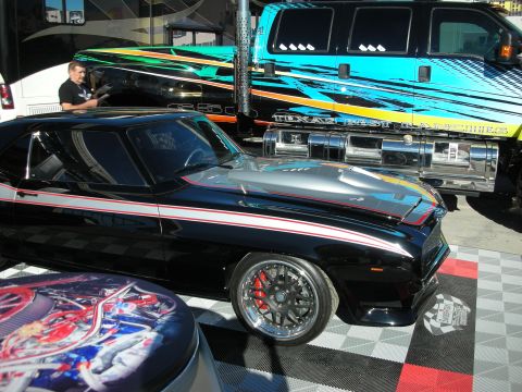 1998 Ford Crown Victoria - A customized classic car is parked next to a large truck with custom graphics at an outdoor event.