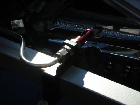 1998 Ford Crown Victoria - Close-up of a red fitting attached to a metal tube, likely part of a fuel or brake line system in an engine bay.