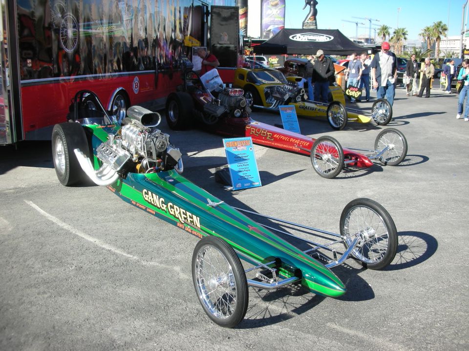 Green dragster with 'GANG GREEN' text, red dragster, and yellow dragster parked outdoors